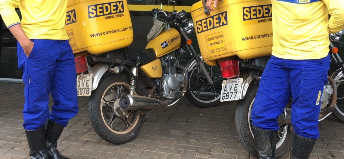 Carteiros dos Correios com motocicleta amarela prontos para entrega, destacando a importância do AADC e adicional de periculosidade.