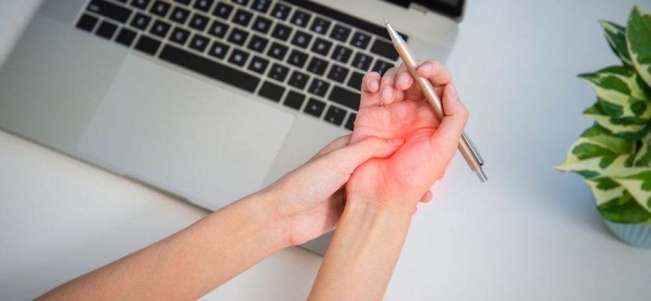 Mão com dor no pulso em frente a um laptop, representando doença ocupacional.